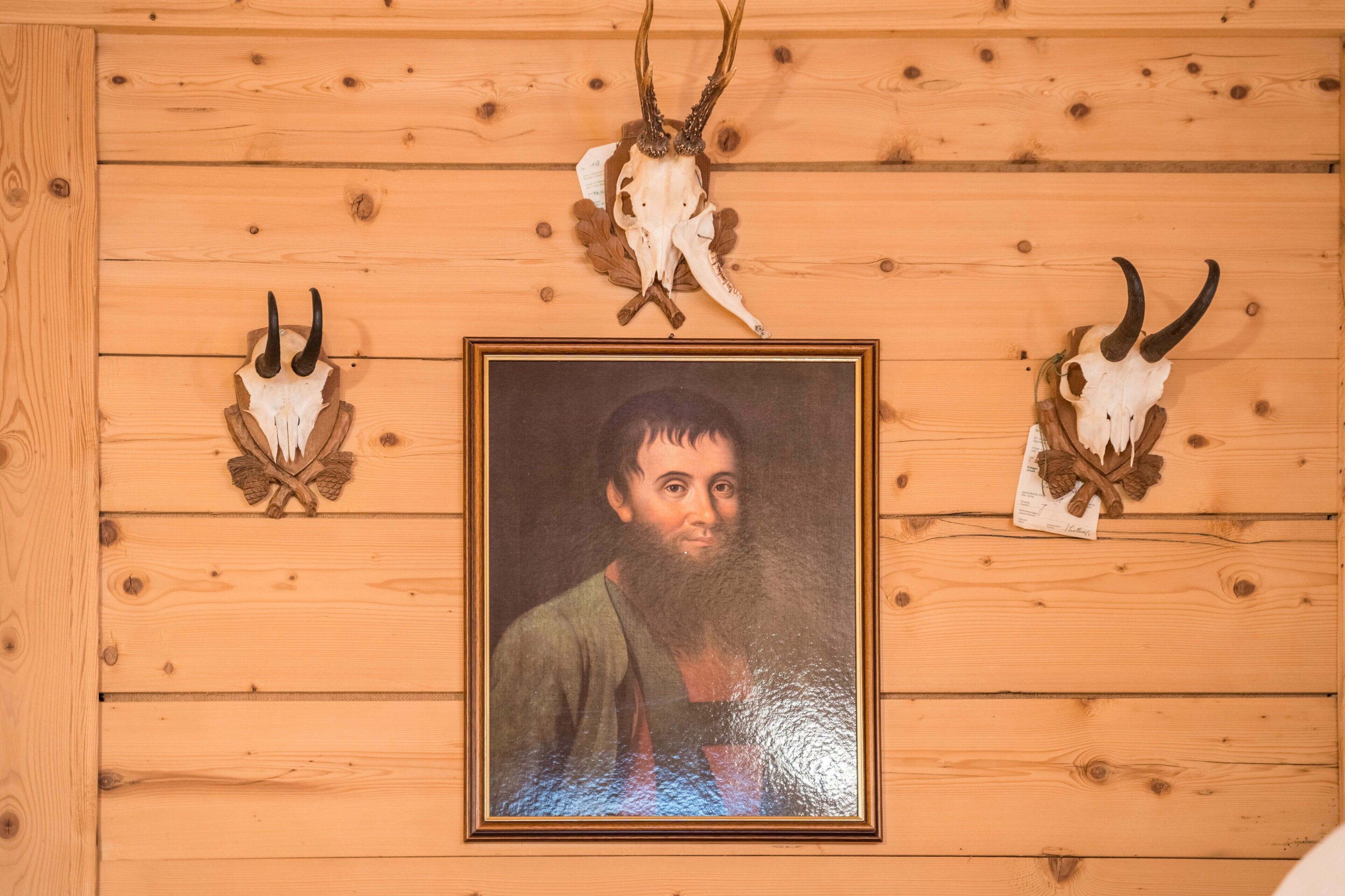 Eine Holzwand mit gerahmtem Porträt und montierten Tierkopfskulpturen.