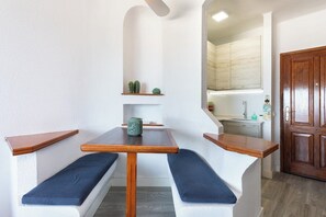 A compact kitchen with white cabinets, a wooden door, and a bench with cushions. - Home2Book Ocean View Paradise with Pool (Adeje)