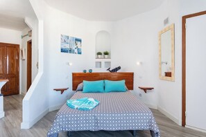 A bedroom with a wooden headboard, a patterned bedspread, two wall-mounted lights, a small shelf with decorative items, and a mirror on the wall. - Home2Book Ocean View Paradise with Pool (Adeje)