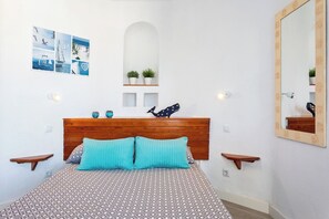 A bedroom with a wooden headboard, a patterned bedspread, two wall-mounted shelves with plants, a wall-mounted mirror, and a wall art piece. - Home2Book Ocean View Paradise with Pool (Adeje)