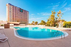 A hotel with a swimming pool, lounge chairs, and a tall building in the background. - Home2Book Ocean View Paradise with Pool (Adeje)