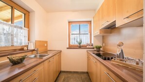 A compact kitchen with wooden cabinets, a sink, a window with a view, and a small potted plant on the windowsill. - Holiday Home “Fichtnhittl” with Mountain View, Wi-Fi, Balcony, Terrace & Garden (Algund)