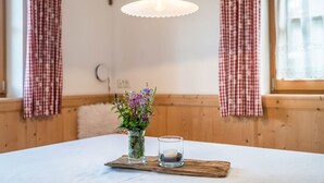 A room with a wooden table, a glass vase with flowers, a candle, and a hanging light fixture. - Holiday Home “Fichtnhittl” with Mountain View, Wi-Fi, Balcony, Terrace & Garden (Algund)