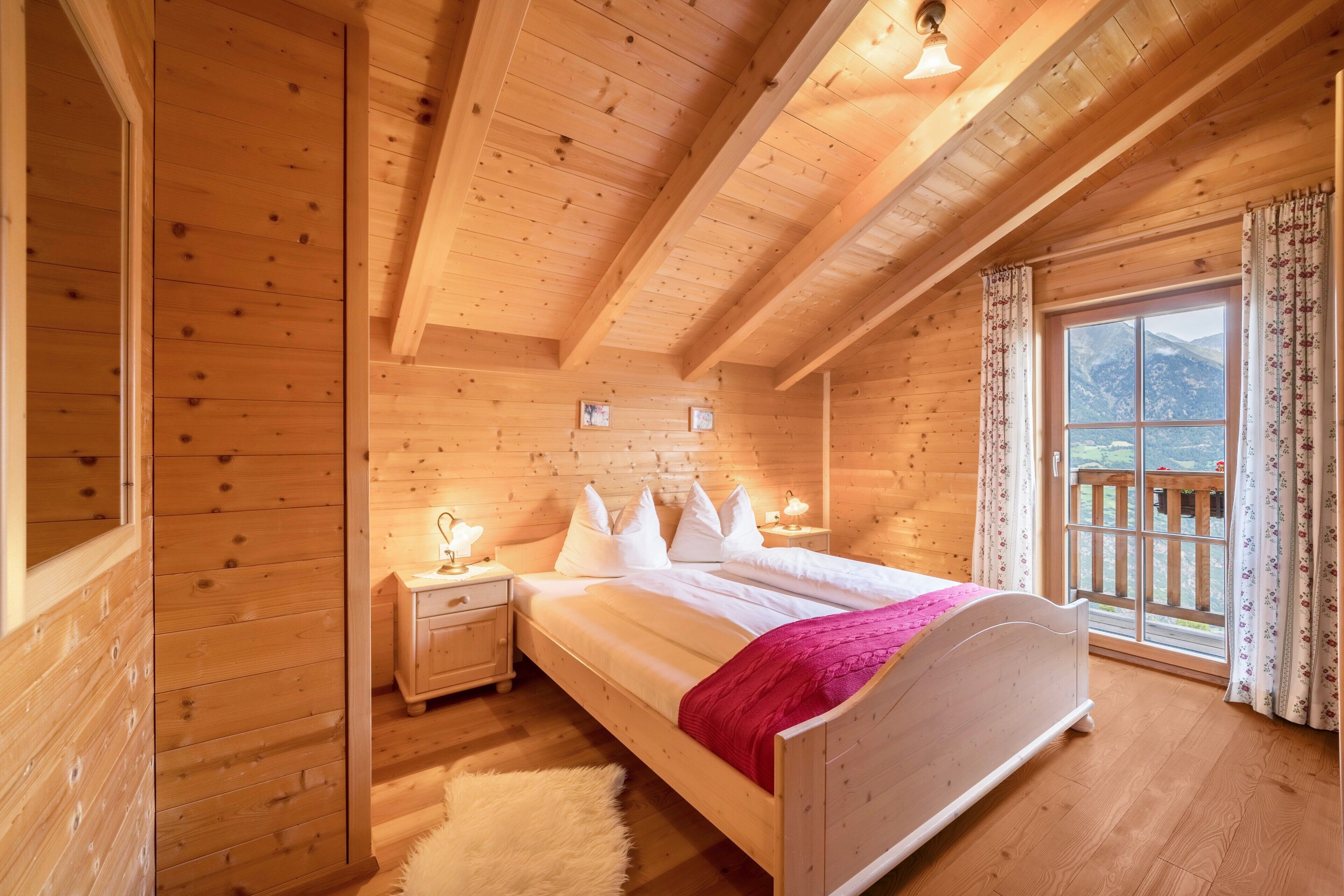Une chambre dans un chalet en bois, avec un lit, des tables de chevet et une fenêtre donnant sur les montagnes.