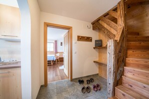 A wooden staircase leading to a room, a hallway with a door to a dining area, and a set of shoes on the floor. - Holiday Home “Fichtnhittl” with Mountain View, Wi-Fi, Balcony, Terrace & Garden (Algund)