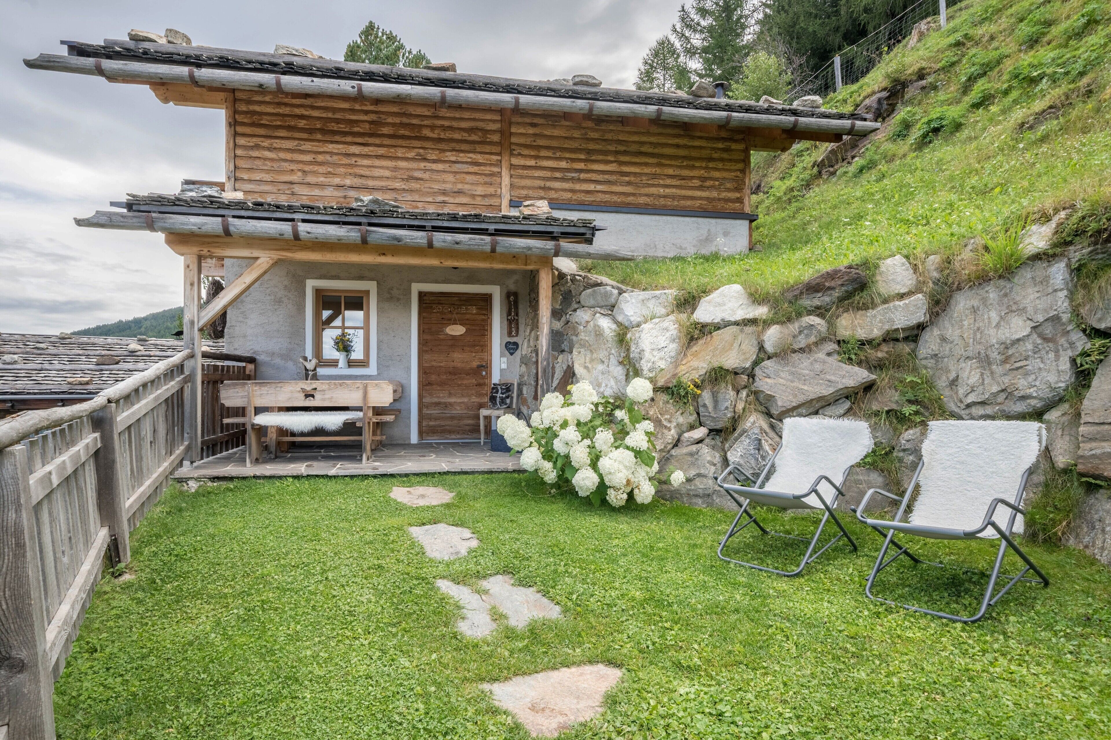 Een rustieke chalet met een stenen muur, houten terras en buiten zitplaatsen.