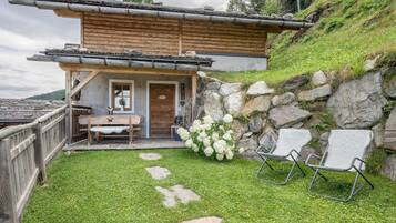 Een rustieke chalet met een stenen muur, houten terras en buiten zitplaatsen.