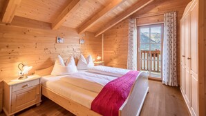 A wooden cabin bedroom with a bed, nightstand, and window with curtains. - Holiday Home “Fichtnhittl” with Mountain View, Wi-Fi, Balcony, Terrace & Garden (Algund)