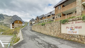A road leading to a hotel with stone walls and wooden balconies, a sign for 'Residence de Tours' and 'Pic du Midi', and mountainous terrain in the background. - Pleasant duplex, parking - 7 guests (La Mongie)