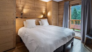 A wooden-paneled bedroom with a large bed, a nightstand, and a window with curtains. - Modern apartment in Courchevel, near slopes (Courchevel 1650)