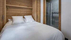 A bedroom with a wooden headboard, a bed with white bedding, and a glass door leading to a balcony. - Modern apartment in Courchevel, near slopes (Courchevel 1650)