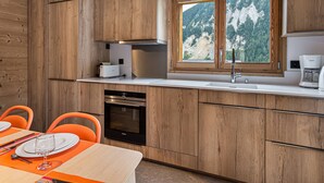 A modern kitchen with wooden cabinets, a built-in oven, and a window with a mountain view. - Modern apartment in Courchevel, near slopes (Courchevel 1650)