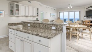 A modern kitchen with granite countertops, white cabinetry, and a dining area with wooden chairs and a table.