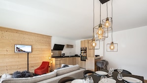 A modern living room with a sofa, a dining table set for four, and a kitchen in the background. - Charming apartment in Courchevel with parking and Wi-Fi included (Courchevel 1650)