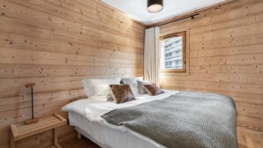 A wooden-paneled bedroom with a bed, bedside table, and a window with a view of buildings. - Charming apartment in Courchevel with parking and Wi-Fi included (Courchevel 1650)