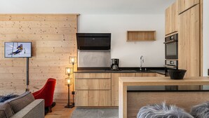 A modern kitchen with wooden cabinetry, a built-in oven, and a large TV mounted on the wall. - Charming apartment in Courchevel with parking and Wi-Fi included (Courchevel 1650)