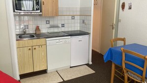 Een kleine keuken met een magnetron, spoelbak, Bosch vaatwasser en een tafel met een blauwe tafelkleed.
