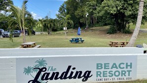A sign for The Landing Beach Resort in Cane Bay, St. Croix, USVI, with picnic tables and palm trees in the background. - Walk to Cane Bay Beach Cottage - End Unit with Mountain Views (Christiansted)