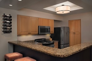 A modern kitchen with wooden cabinets, a granite countertop, a black refrigerator, a microwave, and a pendant light.