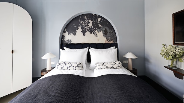 Une chambre avec un grand lit, deux tables de chevet avec des lampes, une armoire et une étagère murale décorée de fleurs.
