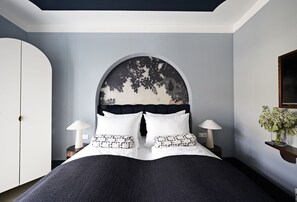 Une chambre avec un grand lit, deux tables de chevet avec des lampes, une armoire et une étagère murale décorée de fleurs.