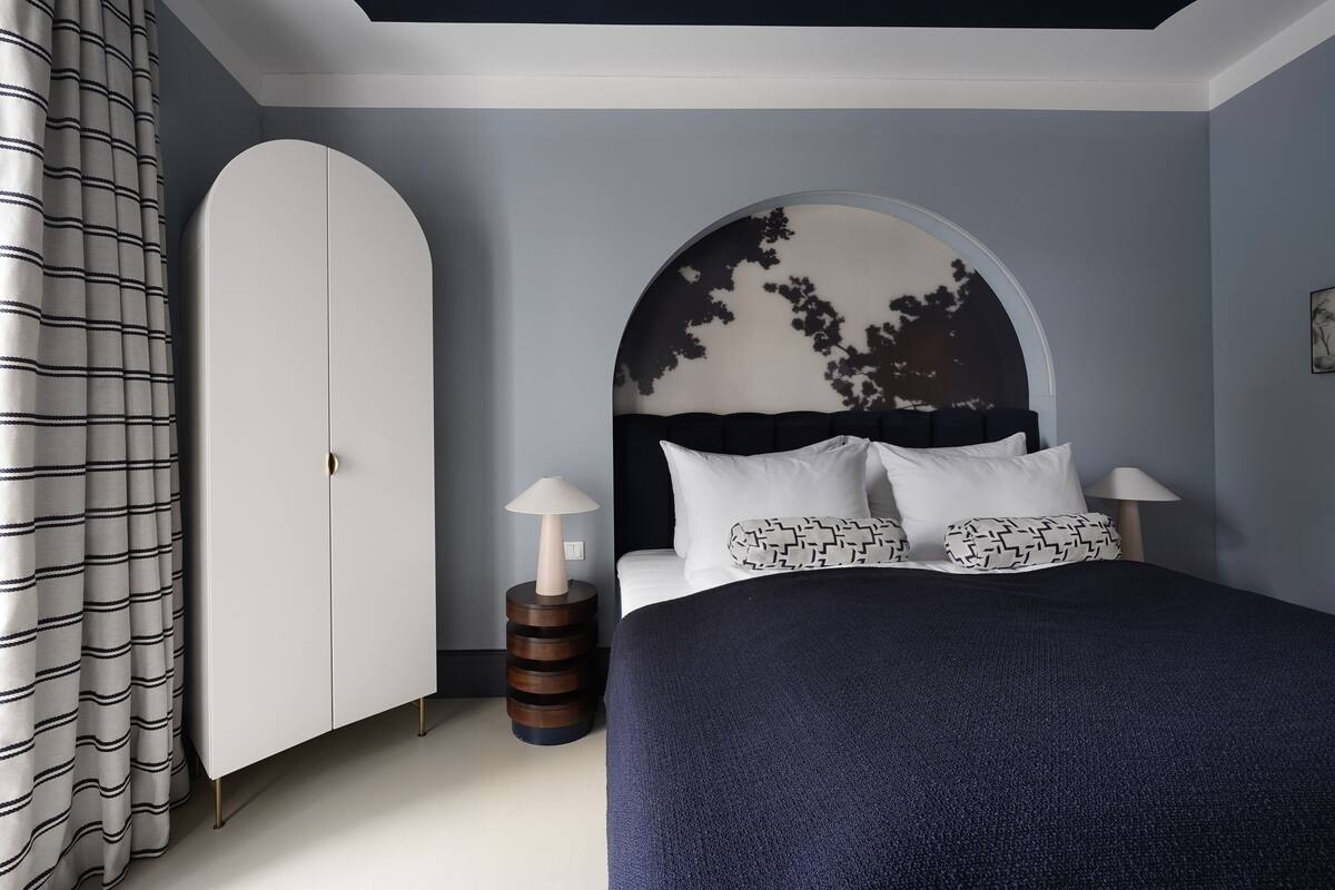 Une chambre à coucher comprenant un lit, une armoire, une petite table ronde et une lampe fixée au mur.