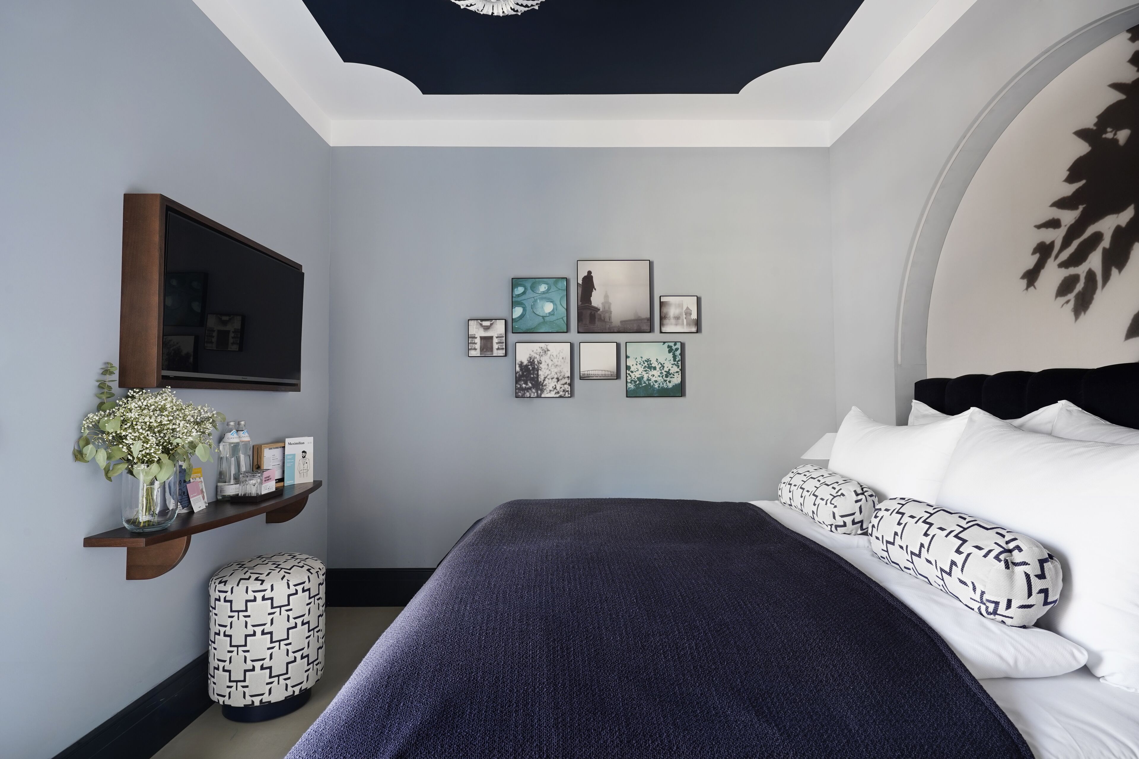 A bedroom with a bed, a shelf with decorative items, and a wall with framed pictures.