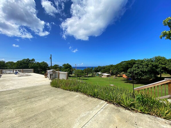 A concrete deck with lounge chairs, a small structure, and a grassy area with trees and a view of the ocean.