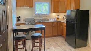 A compact kitchen with wooden cabinets, a black refrigerator, a gas stove, and two bar stools. - Walk to Beach at Cane Bay- Porch Mountain Views, Sea from the backyard (Christiansted)
