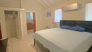 A bedroom with a bed, a ceiling fan, a window with blinds, and a door leading to another room. - Walk to Beach at Cane Bay- Porch Mountain Views, Sea from the backyard (Christiansted)
