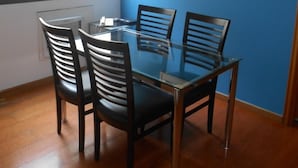 A dining area with a glass table and four chairs, a window with blinds, and a blue wall with a framed abstract painting. - Ipanema Beach (Rio de Janeiro)
