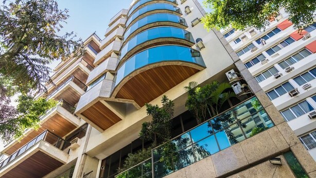 A multi-story building with a modern architectural design, featuring balconies with wooden railings and a prominent blue glass facade. - Ipanema Beach (Rio de Janeiro)