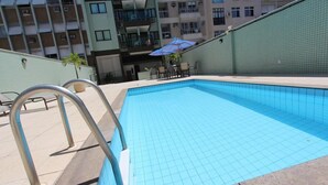 A swimming pool with tiled flooring and metal handrails, surrounded by a building with balconies and a tiled exterior wall. - Ipanema Beach (Rio de Janeiro)