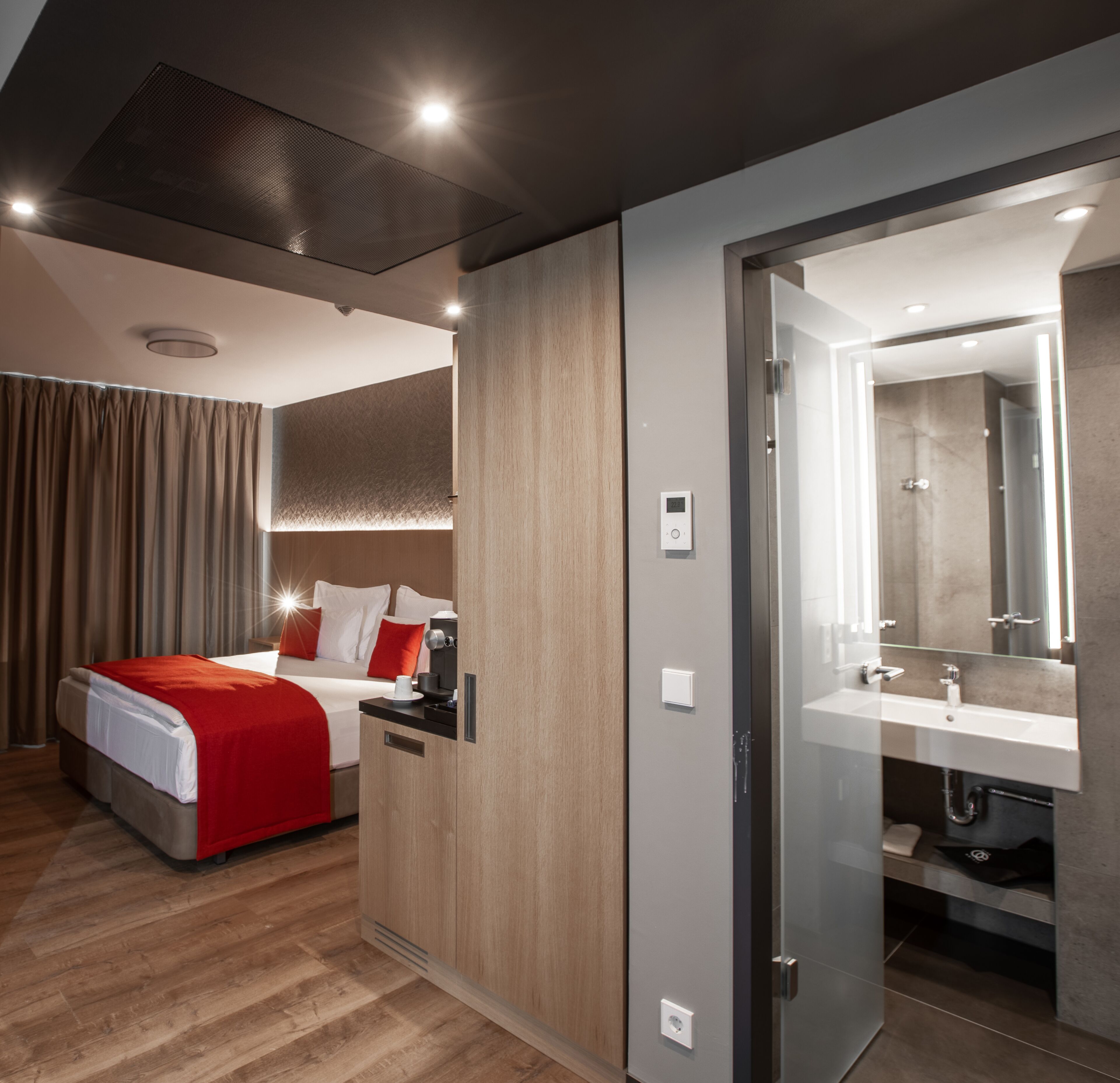 Une chambre d’hôtel moderne équipée d’un lit, d’une table de chevet et d’une salle de bain avec un lavabo et un miroir.