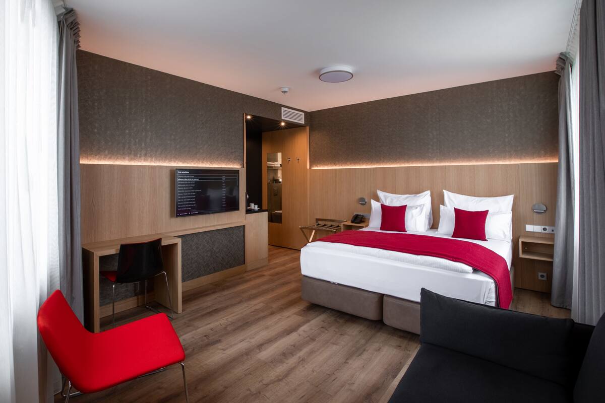 A modern hotel room with a large bed, a desk, and a TV.