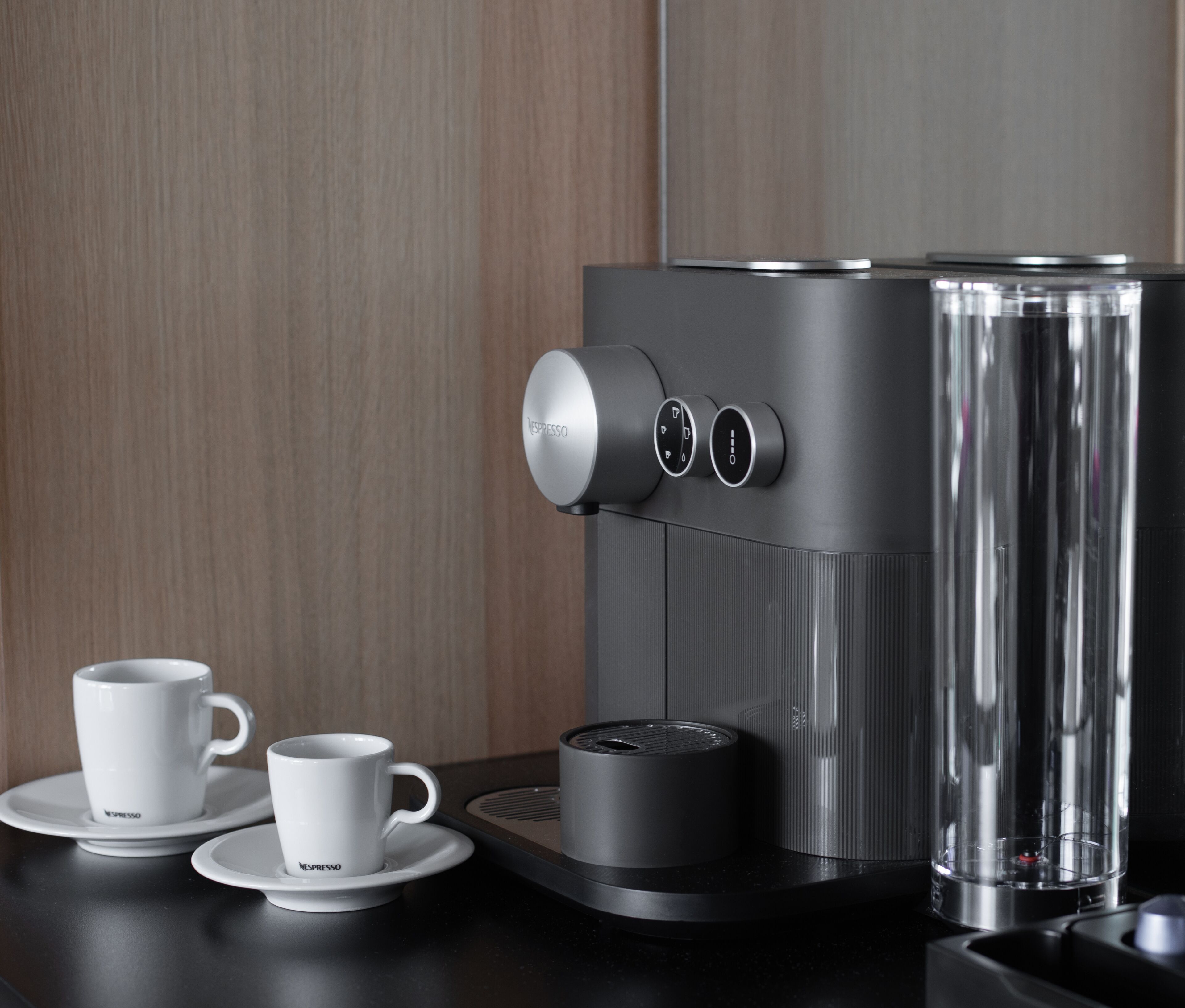 Una cafetera espresso moderna con dos tazas sobre platillos, un depósito de agua y un panel de control.