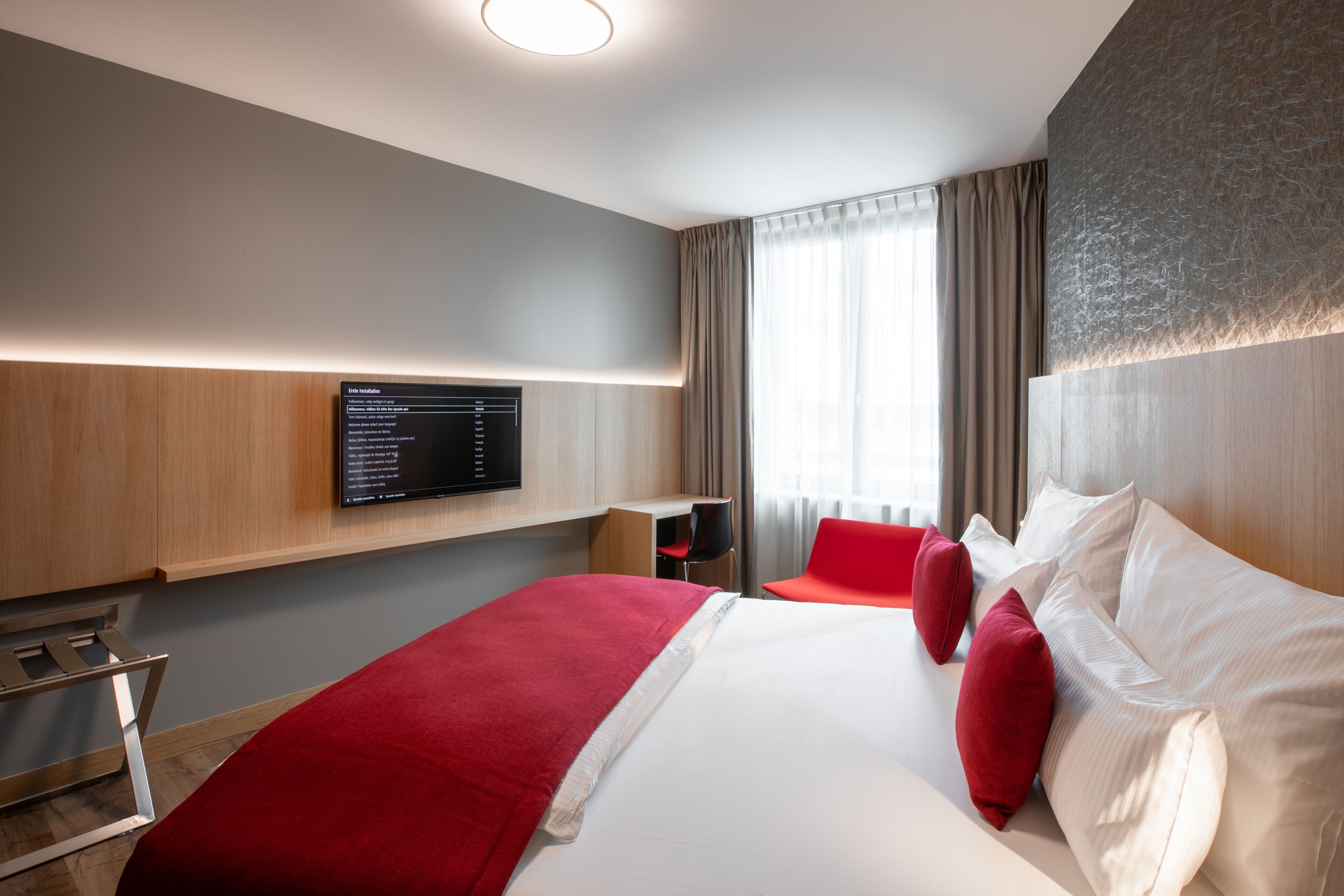 Ein modernes Hotelzimmer mit einem großen Bett, einem Schreibtisch und einem an der Wand befestigten Fernseher.