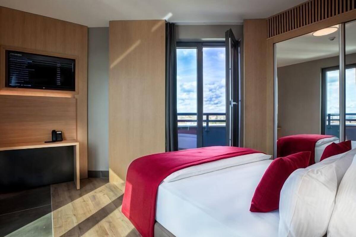 A hotel room with a bed, a TV, a balcony, and a large mirror.