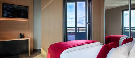 A modern hotel room with a bed, a desk, a TV, and a balcony with a view.