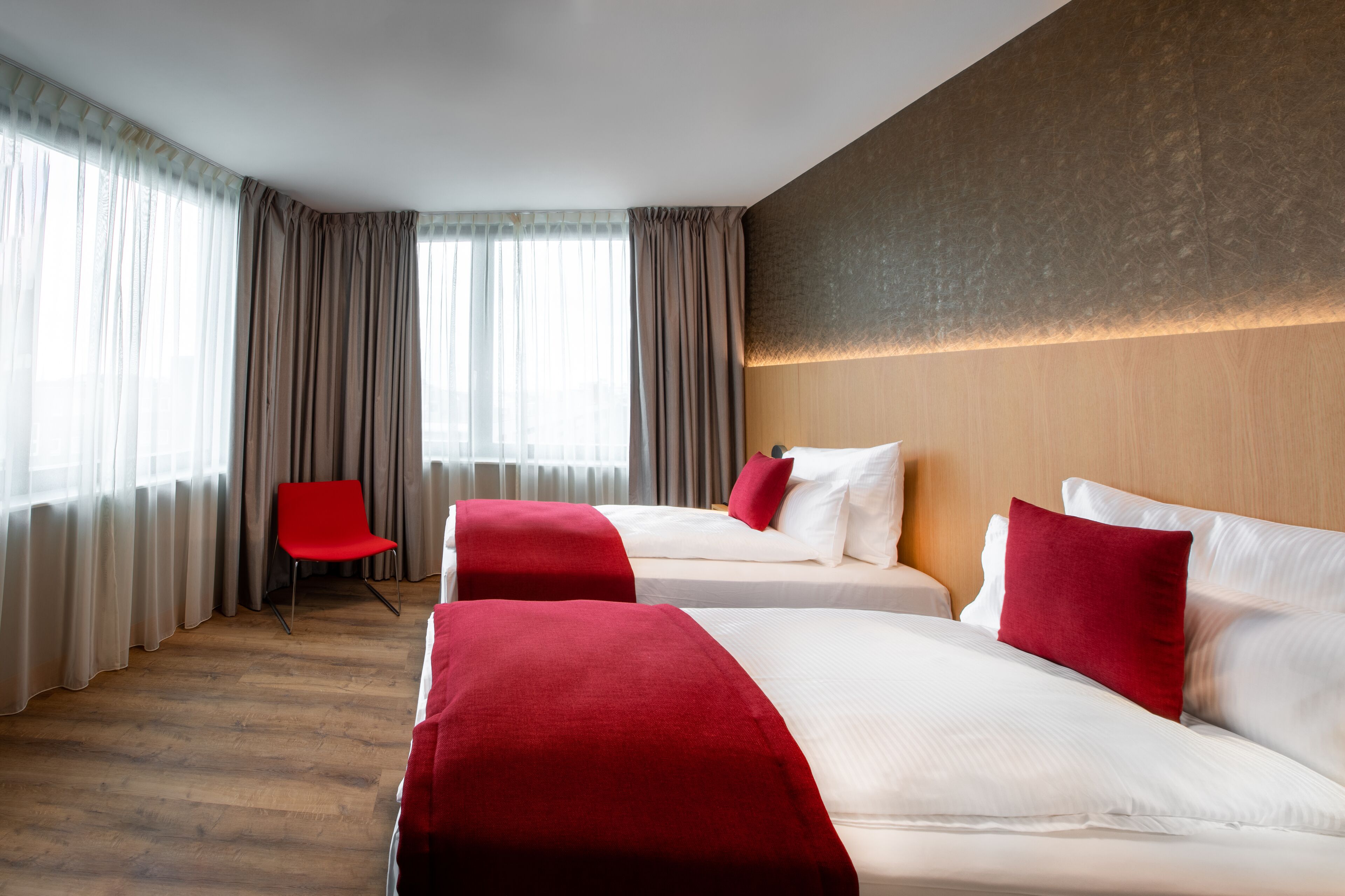 A hotel room with two beds, a red chair, and a large window with curtains.