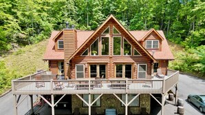 A log cabin with a balcony, stone foundation, and a car parked nearby. - #1 PRVT. BLACK-MT. LUX LOG ESTATE. / HOT TUB / GAME RM / PETS / 2 FIRE PL. 6/6.5 (Black Mountain)