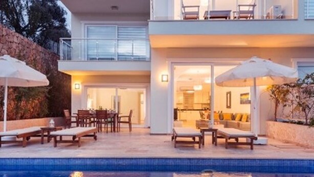 Una casa moderna de dos pisos con piscina, mobiliario exterior y un balcón.