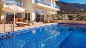 Un edificio moderno de dos pisos con piscina, mobiliario exterior y vistas a montañas.