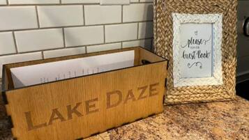 Une boîte en bois portant l’inscription « LAKE DAZE » est posée sur un plan de travail de cuisine, à côté d’un panier en osier sur lequel est accroché un panneau indiquant : « Veuillez inscrire votre nom dans notre livre d’or ».