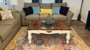 A living room with a beige sofa, colorful cushions, a wooden coffee table, and a patterned rug.