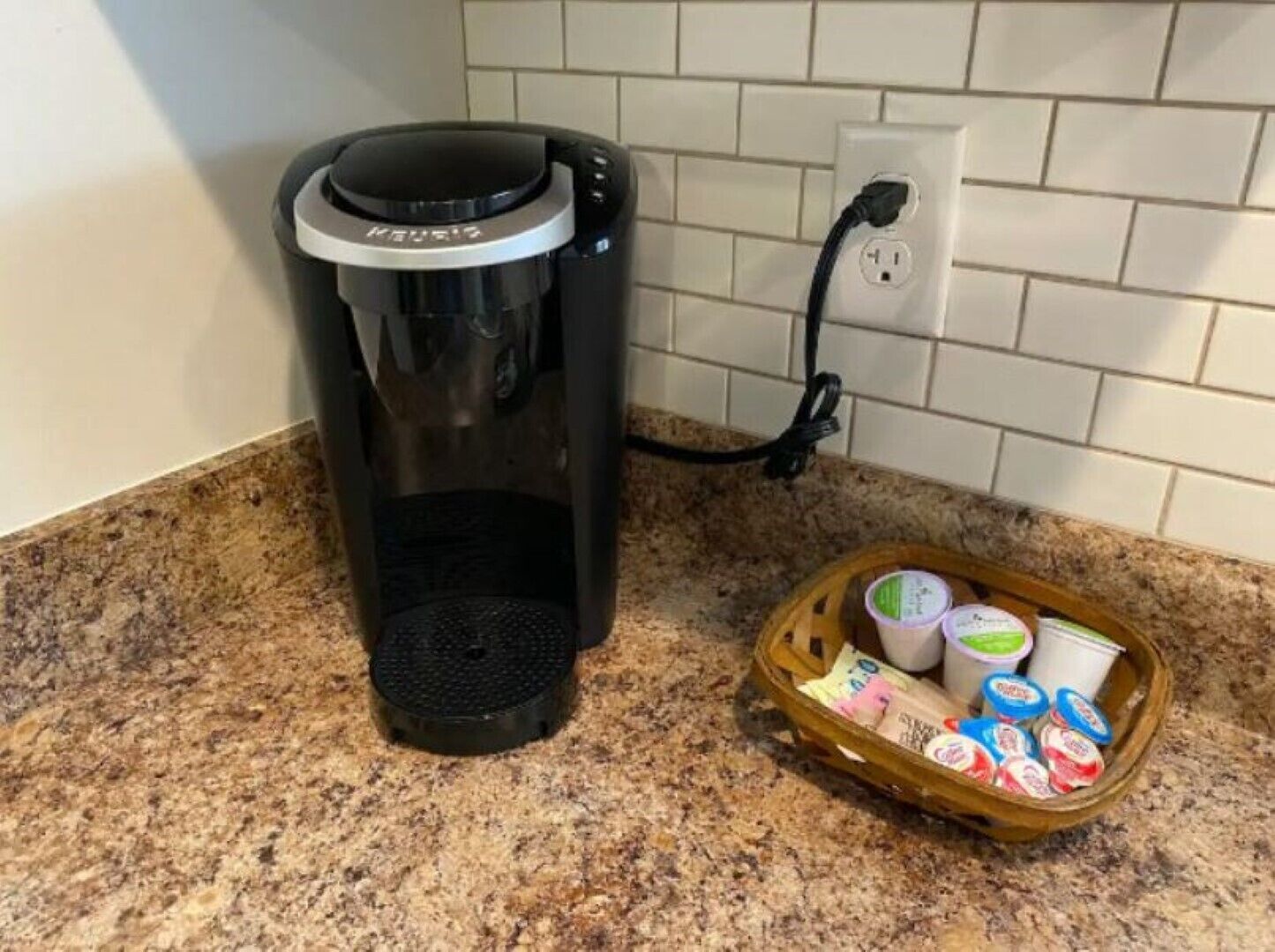 Uma cafeteira Keurig em uma bancada de cozinha, com uma cesta de potes de iogurte.