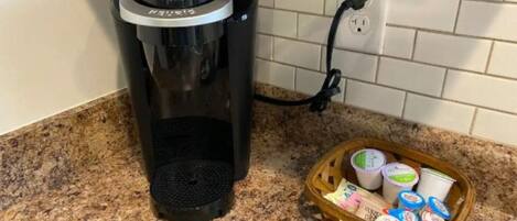 Uma cafeteira Keurig em uma bancada de cozinha, com uma cesta de potes de iogurte.