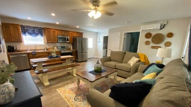 A modern kitchen with wooden cabinets, a dining table, and a bench. There is a living area with a sofa and a coffee table.