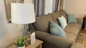 A living room with a sofa, a lamp, a small table with a plant, and a framed picture.