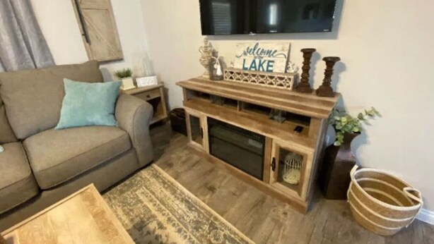 A living room with a sofa, coffee table, TV mounted on the wall, and a sign that says "Welcome to Lake".